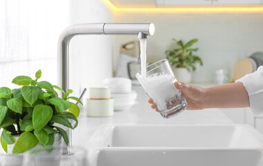 Woman filling glass with water from tap in kitchen, closeup