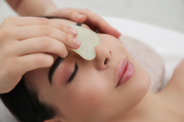 Obraz na płótnie Canvas Young woman receiving facial massage with gua sha tool in beauty salon, closeup