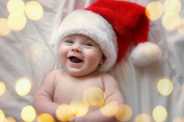 Smiling Baby Wearing Red Santa Claus Hat Celebrating Christmas. Cute Newborn Baby In Christmas Hat Lying On White Blanket. Merry xmas, Happy New Year, Infants, Holidays Concept. Funny Little Child.