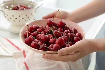 Woman holding bowl with fresh ripe cherries in kitchen, closeup - Powered by Adobe