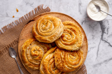 Homemade traditional Serbian rolled pie with cabbage and sour cream on a marble background served on a round wooden board in a rustic style top view horizontal 