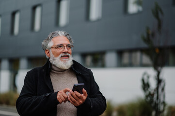 Portrait of a senior businessman using smartphone outside of the office building