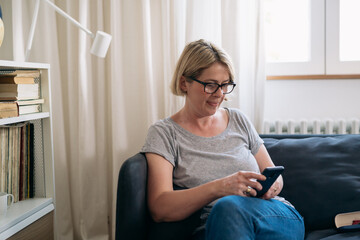 Obraz premium mid adult woman sits on sofa in living room and using mobile phone