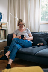 Obraz premium mid adult woman sits on sofa in living room and using mobile phone