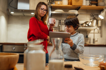mother and son prepares food in kitchen. checking recipes on digital tablet