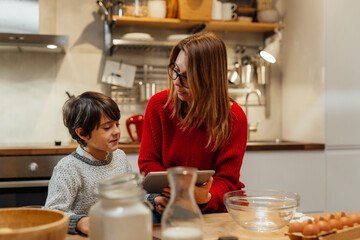 mother and son prepares food in kitchen. checking recipes on digital tablet