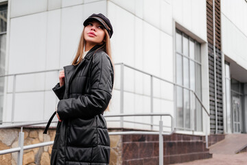 Elegant young woman in black coat and beret standing near office building looking away outdoor