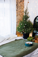 New Year's gifts in paper and bright ribbons under the Christmas tree on the floor on New Year's Eve. A Christmas tree decorated with toys stands by the bed