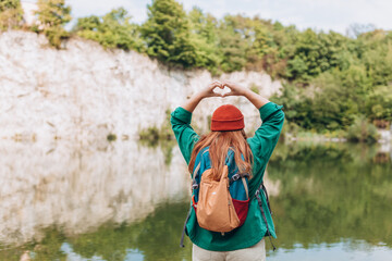 Woman in hat hiking in woods. Adventure women enjoying view of majestic mountain lake explore travel. Freedom and active lifestyle concept. Girl making by hands in shape of love heart.