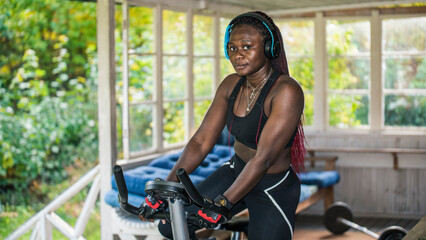 Fototapeta na wymiar African woman exercising at home outdoors on an exercise bike during autumn