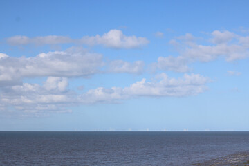 Wind farm on horizon at sea with dark blue sea below and pale blue sky above