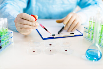 Close-up hands of a researcher in a lab dripping a blood sample in a Petri dish. Focus on a pipette.