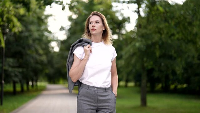 self-confident woman is walking alone in city park in summer, medium portrait in movement