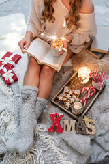 The girl is sitting in a christmas atmosphere, drinking a hot drink and reading a book