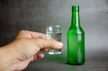 soju bottle on grey background with hand, selective focus