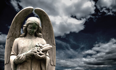An ancient statue of guardian angel against dramatic view of cloudy sky. Copy space.