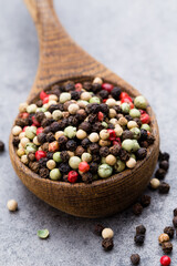 Peppercorn mix in a wooden bowl on grey table.