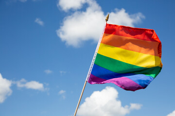 Regenbogenflagge vor blauem Himmel mit Wolken als symbolischer Hintergrund