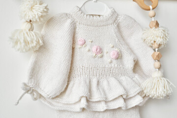 Knitted dress with embroidery on hanger on shelf, kids clothes and accessories. Needlework and knitting. Hobbies and creativity. Knit for children. Handmade