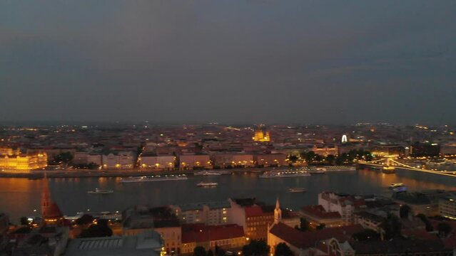 Panoramic scene from over the Fisherman's Bastion showing bridges over the Danube River and Parliament lighted up in the evening as city cruise ships sailing in the water