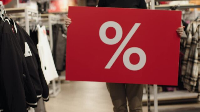 female dancing with red percent label banner in hands sale in shop discount sales clothing store. rows of clothes advertising sales discounts big deals for black friday sale off. prices dropping