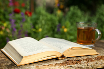Open book with glass cup of tea on wooden table in garden