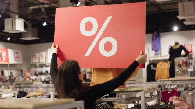 woman seller install red percent off label sale hands of mannequin clothes store shop mall. shopping discounts label sellout selloff in clothing shop. black friday concept. percent sign on red card