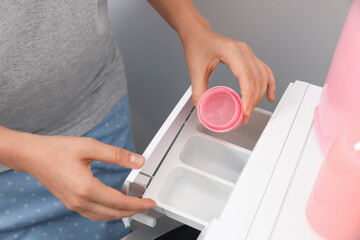Woman pouring laundry detergent into drawer of washing machine, closeup