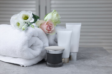 Towels, cosmetic products and flowers on grey table indoors