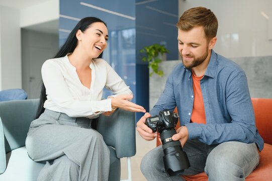 Photographer in office shows photo model in camera. Consultant adjusts activities company as whole. Photo session employees in workplace. Manager well-executed project. Photos best employees company.