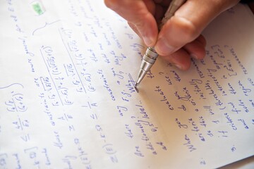 Student writing mathematical calculations on paper, closeup