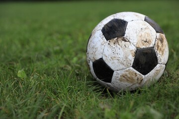 Dirty soccer ball on green grass outdoors, closeup. Space for text