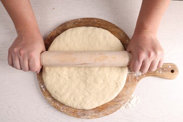 Man rolling dough with wooden pin at white table, top view