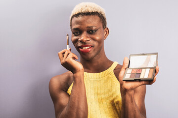 An african boy posing on a purple background while showing cosmetics, androgynous concept.