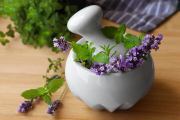 Mortar with fresh lavender flowers, herbs and pestle on wooden table