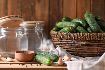 Fresh cucumbers and other ingredients near empty jars prepared for canning on wooden table