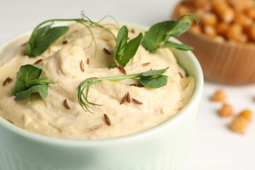 Bowl of tasty hummus with pea leaves on white table, closeup