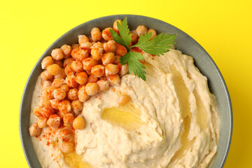 Bowl of tasty hummus with chickpeas and parsley on yellow background, top view