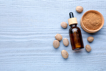 Bottle of nutmeg oil, nuts and powder on grey wooden table, flat lay. Space for text