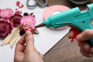 Woman using hot glue gun to make craft at wooden table, closeup