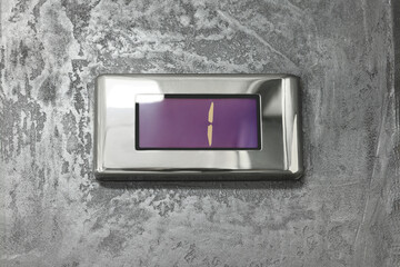 Elevator floor indicator with number one on grey textured wall, closeup