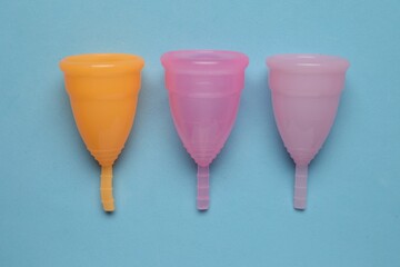 Different menstrual cups on light blue background, flat lay. Reusable female hygiene product
