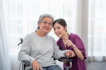 Obraz premium Asian young nurse taking care and talking mature female patient sitting on wheelchair in hospital. Healthcare concept.