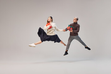 Flexible dancers, young happy couple in warm winter clothes dancing with festive gift boxes over...