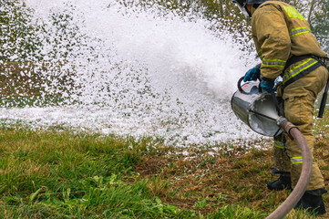 A firefighter in protective clothing extinguishes a fire by feeding foam. A firefighter...