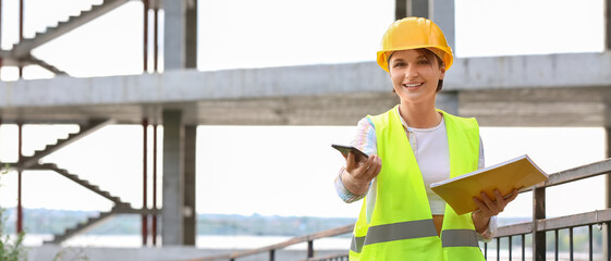 Female construction worker with folder and mobile phone at site