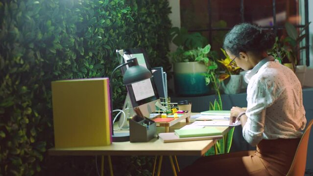 Woman web designer, planning, and music at agency office writing strategy notes for online night project. Paperwork, documents and creative girl freelancer with notebook, graph and chart