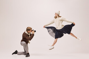 Young stylish photographer taking picture of graceful young ballerina isolated on grey background....