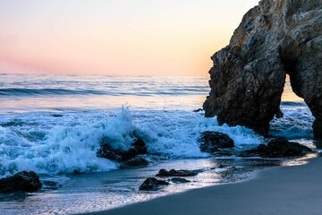 Closeup of a rocky El Matador sea beach with water waves making a foam at sunset