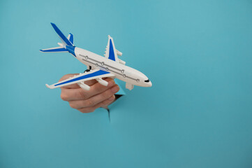 Fototapeta na wymiar A female hand sticking out of a hole from a blue background holds a model of an airplane. 